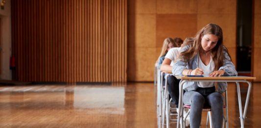 Prüflinge an Einzeltischen in einer Schulaula.