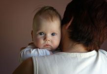 Ein Baby schaut über den Rücken seiner Mutter.