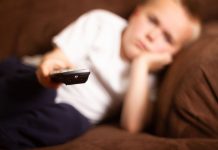 Bericht: Corona-Krise beeinträchtigt Kindergesundheit – Spätfolgen (Long-Covid) möglich Ein Junge auf dem Sofa liegend richtet eine ernbedienunge aus dem Bild heraus.