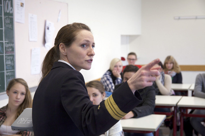 Junge Frau in Marineuniform doziert in einer Schulklasse.