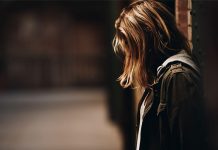 Ein Mädchen lehnt an einem Eisenträger in einem schwach beleuchteten Korridor.