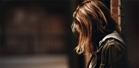 Ein Mädchen lehnt an einem Eisenträger in einem schwach beleuchteten Korridor.