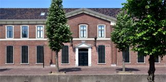 Schullandschaft im Wandel: Bürgerentscheid in Ostfriesland sorgt für Unsicherheit Ein relativ niedriges, breites zweistöckiges Backsteingebäude aus dem 19. Jahrhundert mit hervorgehobenem Portikus an einer klinkergepflasterten Straße hinter einem kleinen Kanal, davor drei Bäume.