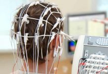 Junge mit Elektroden am Kopf von hinten, im Hintergrund Apparaturen und ein Bildschirm