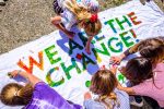 Jugendliche schreiben "we are the change" auf ein Plakat.