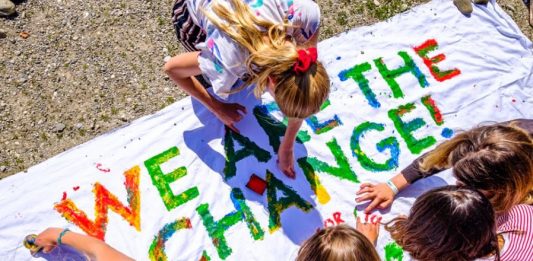 Jugendliche schreiben "we are the change" auf ein Plakat.