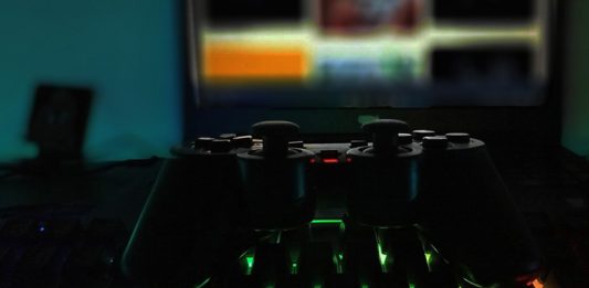 Gamepad auf einer Tastatur mit grüner Beleuchtung, im Hintergrund ein Bildschimr