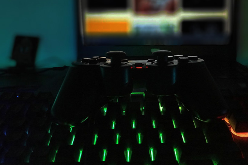 Gamepad auf einer Tastatur mit grüner Beleuchtung, im Hintergrund ein Bildschimr