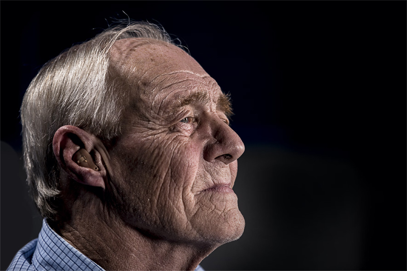 Ein hochbetagter, schräg nach oben blickender, lächelnder Mann im Profil vor schwarzem Hintergrund.