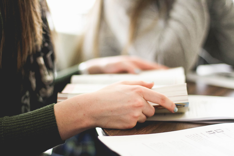 Zwei junge Frauen an einem runden Tisch mit Büchern und multiple choice test darauf.