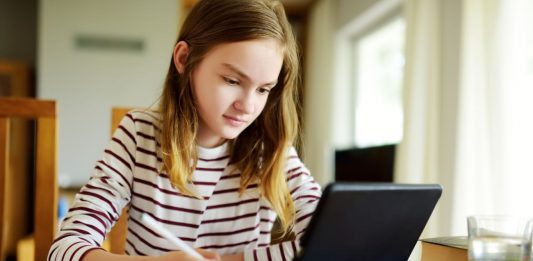 sitzendes Mädchen das auf einen Bildschirm schaut und Notizen macht