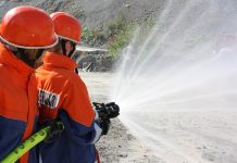 Zwei Jugendliche in Feuerwehruniformen halten einen Feuerwehrschlauch vor einem Sandhügel