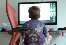 Ein junge auf einem Schreibtischstuhol sieht aus Untersicht auf eine Bildschir