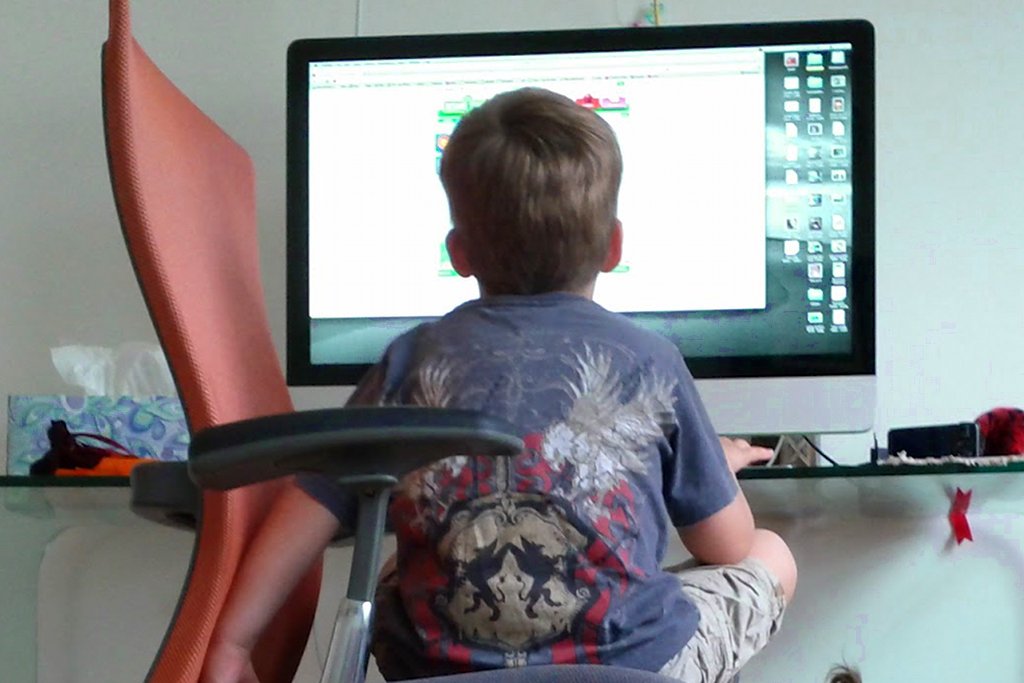 Ein Junge auf einem Schreibtischstuhl sieht aus Untersicht auf eine Bildschir