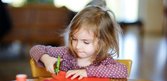 Kindergartenkind an einem Tisch zerschneidet buntes Papier