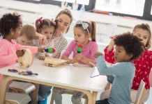 VBE mahnt, die Kitas in der Corona-Krise nicht länger zu übersehen Erzieherin musiziert mit sechs Kindern an einem Tisch