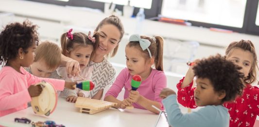 Erzieherin musiziert mit sechs Kindern an einem Tisch