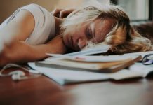 Eine junge blonde Frau schläft auf Unterlagen gesunken auf einem Schreibtisch.