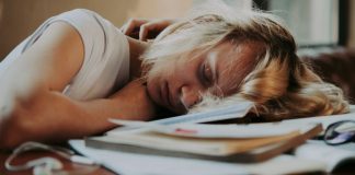 Eine junge blonde Frau schläft auf Unterlagen gesunken auf einem Schreibtisch.