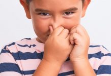 grinsender Junge hält sich die Nase zu.