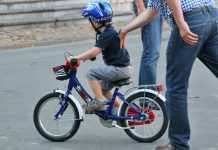 EIn Mann in kariertem Hemd schiebt ein kleines Kind auf dem Fahrrad an.