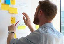 Junger bärtiger Mannn im Hemd ordnet Notizzettel an einer Metaplan Wand