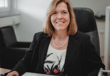 Eine Frau gekleidet in T-Shirt und Jacket in einem Bürostuhl schaut lächelnd aus dem Bild heraus.