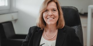 Eine Frau gekleidet in T-Shirt und Jacket in einem Bürostuhl schaut lächelnd aus dem Bild heraus.