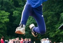 Beine eines Weitspringers in der Luft vor zusehender Schülergruppe