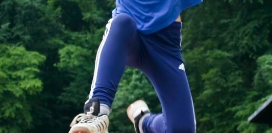 Beine eines Weitspringers in der Luft vor zusehender Schülergruppe