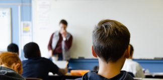 Jugendliche in einem Klassenraum, Blick von hinten auf einen Lehrer.