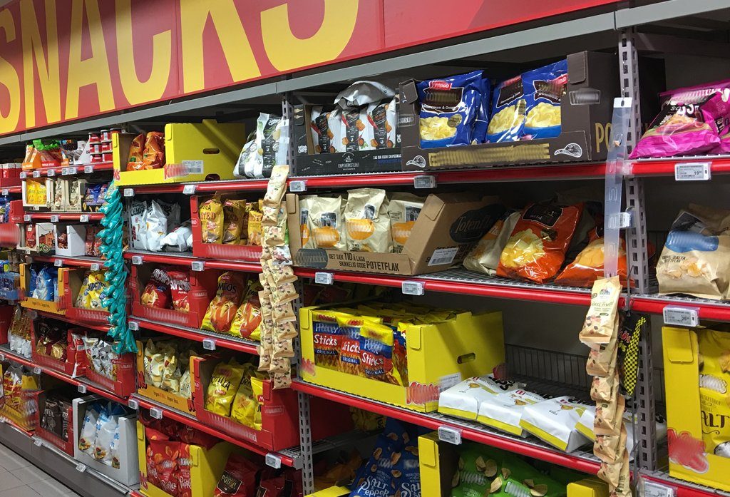 Es gibt viele Snacks im Supermarktregal und die Konkurrenz ist hart. Werbung ist da von großer Bedeutung für die Hersteller. Foto (Extra (Coop supermarket) Bergen Storsenter Norway 2017-11-16 snacks aisle): Wolfmann / Wikimedia Commons (CC BY-SA 4.0) (Ausschnitt mit verwischten Schriftzügen)