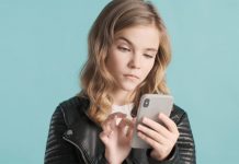 Langhaariges Mädchen vor blauem Hintergrund tippt mit skeptischem Blick auf ihr Smartphone.