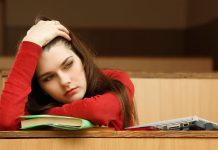 Studentin im Hörsaal blickt erschöpft über Bücher hinweg