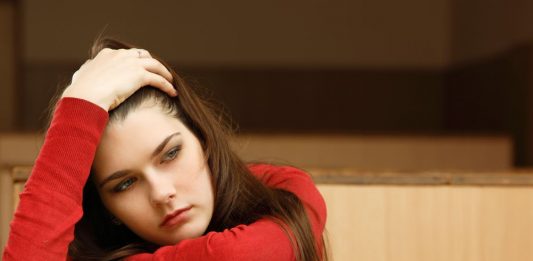 Studentin im Hörsaal blickt erschöpft über Bücher hinweg