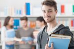 Ein Student schaut in die Kamera, hinter ihmverschwommen eien Lerngruppe in einer Bibliothek