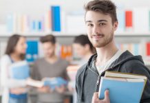Ein Student schaut in die Kamera, hinter ihmverschwommen eien Lerngruppe in einer Bibliothek