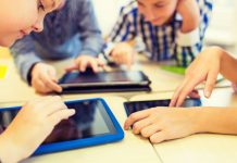 Junge Schüler beugen sich über bunte Tablets auf eine Tischgruppe.