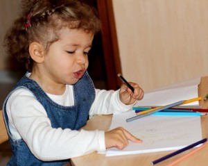 kleines Mädchen mit Buntstiften an einem Zeichentisch