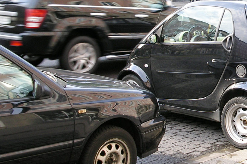 Längs- und querparkende Autos an einer Straße auf der ein weiteres Auto vorbeifährt.