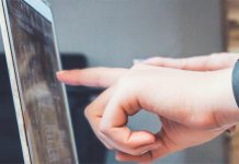 Finger zweier Hände deuten auf ein unerkennbares Detail auf einem Laptopbildschirm