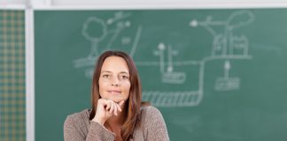 “Wachstumsorientierte Denkweise”: Welche Lehrkräfte von Schülern gemocht werden EIne Frau in graubraunem Pullover, mit langen, roten Haaren, das Kinn an die stifthaltende Hand gestützt sitzt an einem Pult. Hinter ihr verschwommen eine Tafel mit einer technische anmutenden Zeichnung.