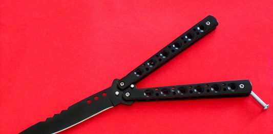 aufgeklapptes schwarzes Butterflymesser auf rotem Grund