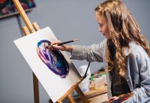 Schülerin malt einen bunten Kreis auf ein Blatt, das auf einer Staffelei steht.