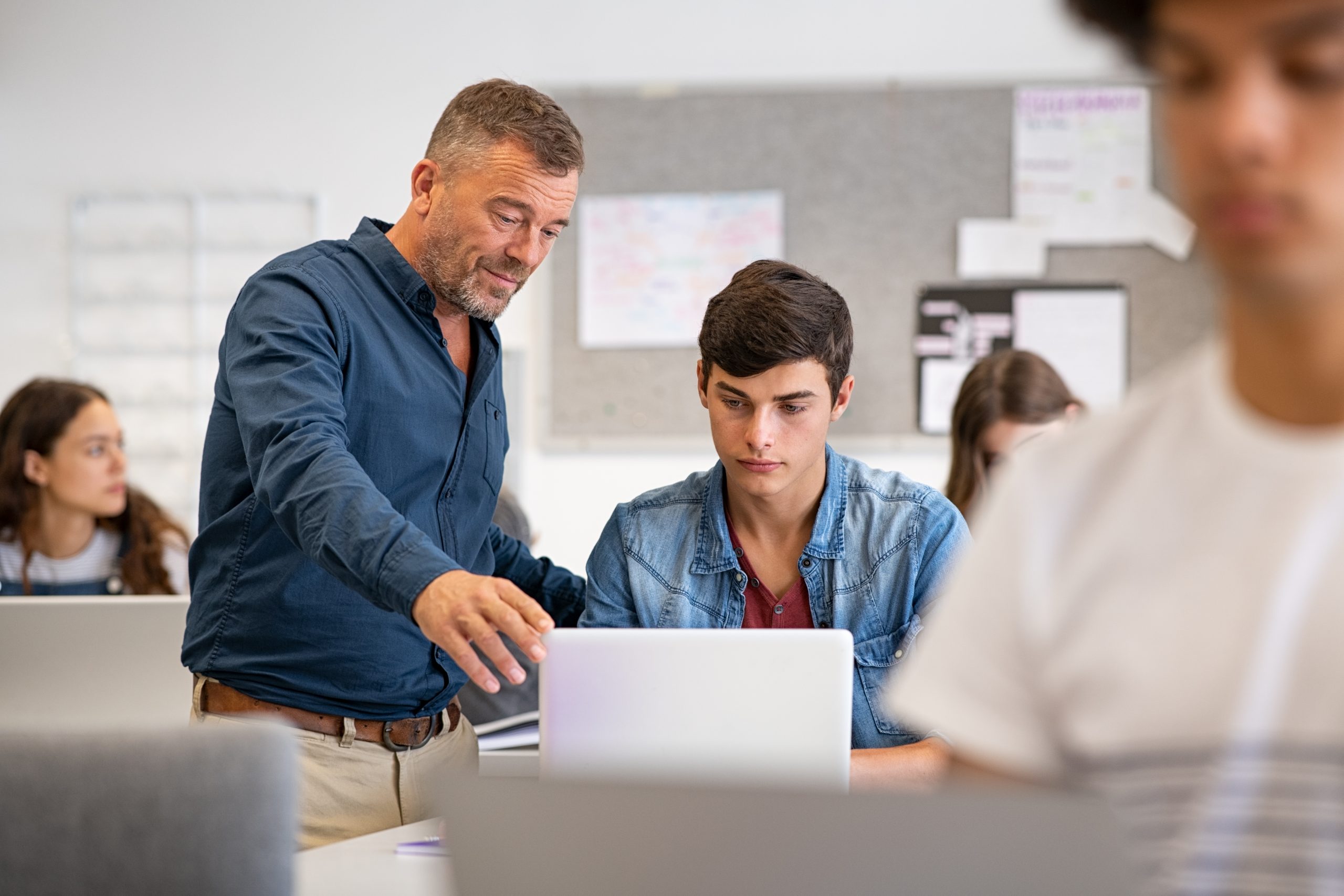 Ein Lehrer schaut mit einem Schüler geminesam auf ein Laptop.