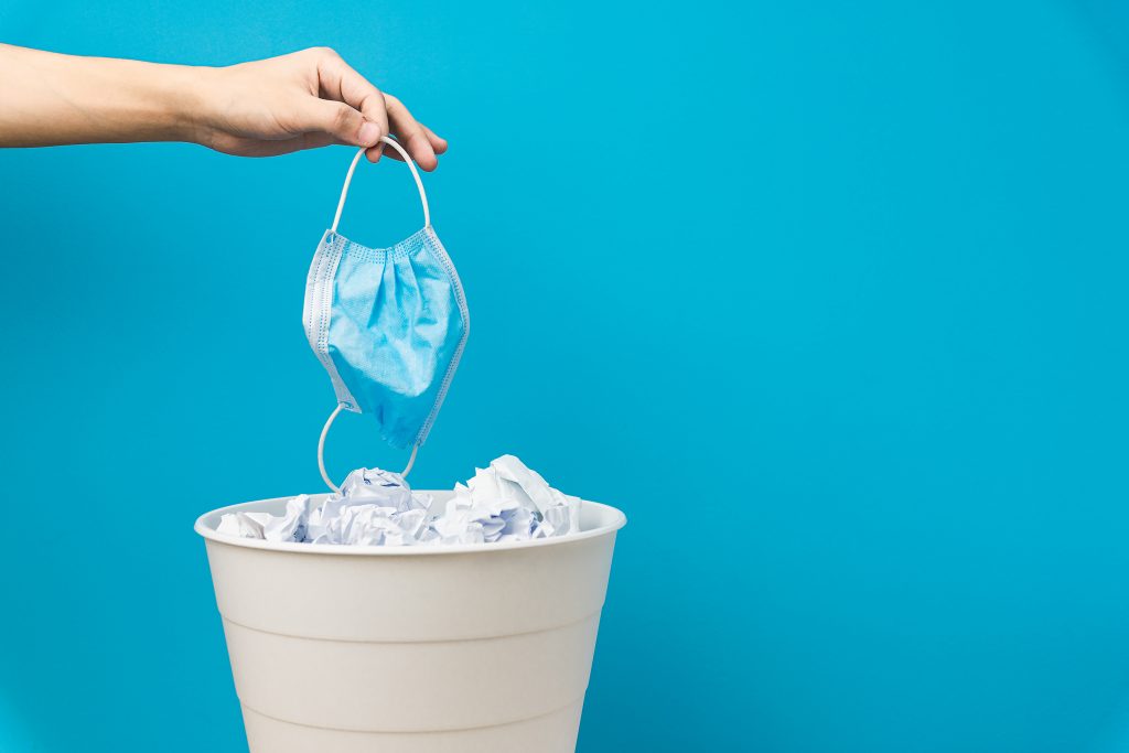Eine Hand wirt eine medizinische Maske in den Mülleimer