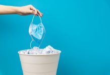 Eine Hand wirt eine medizinische Maske in den Mülleimer