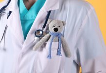 Arzt (Torso) mit einem gehäkelten Teddybär in der Brusttasche