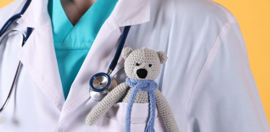 Arzt (Torso) mit einem gehäkelten Teddybär in der Brusttasche