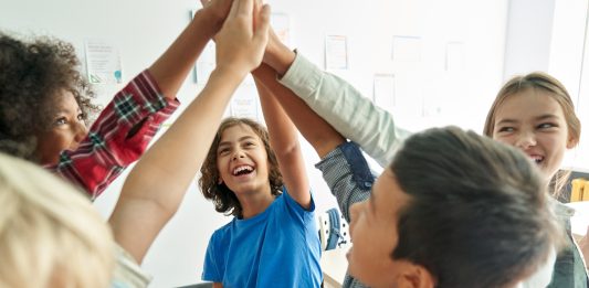 6 fröhliche Kinder im Kreis klatschen triumphierend die Hände zusammen.